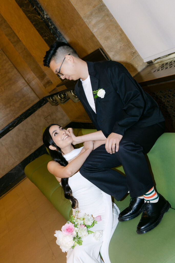 Bride reclining on the green couch while holding hands with the groom during their Manhattan City Hall wedding.