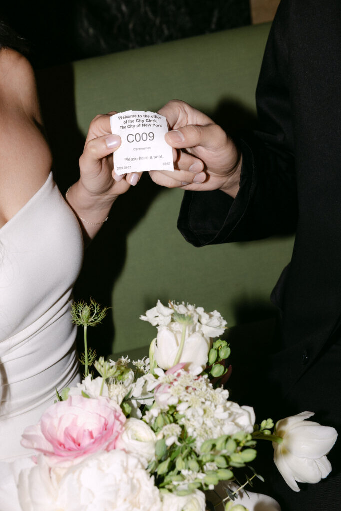 Newlyweds holding a City Hall marriage token beside the bride’s bouquet during their Manhattan City Hall wedding.