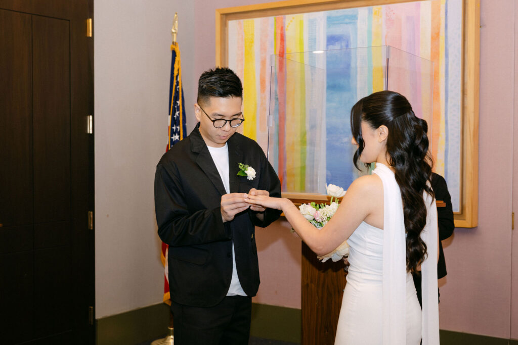 Groom placing a wedding ring on the bride’s finger during their Manhattan City Hall wedding ceremony.
