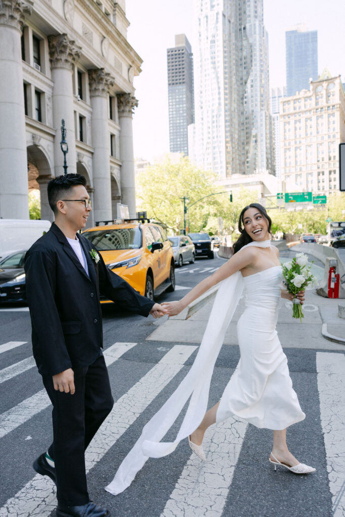 Newlyweds holding hands and laughing in a Lower Manhattan crosswalk after their City Hall wedding.