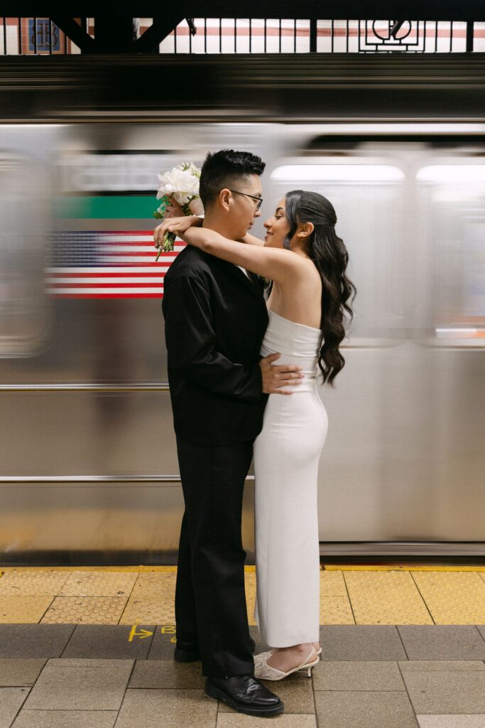 Newlyweds embracing on a subway platform as a train passes after their Manhattan City Hall wedding.
