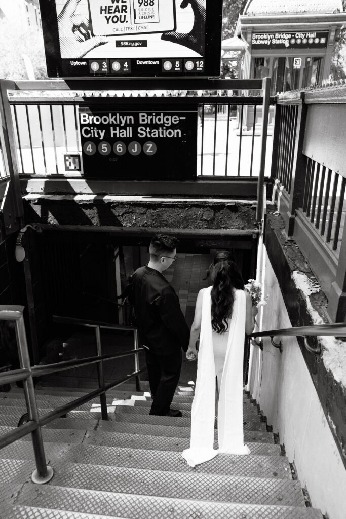 Newlyweds holding hands while walking down the Brooklyn Bridge–City Hall subway stairs after their wedding.