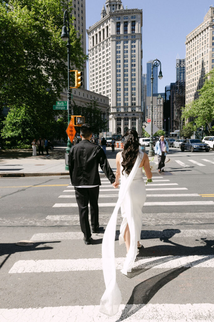 Newlyweds holding hands and crossing Worth Street after their Manhattan City Hall wedding.