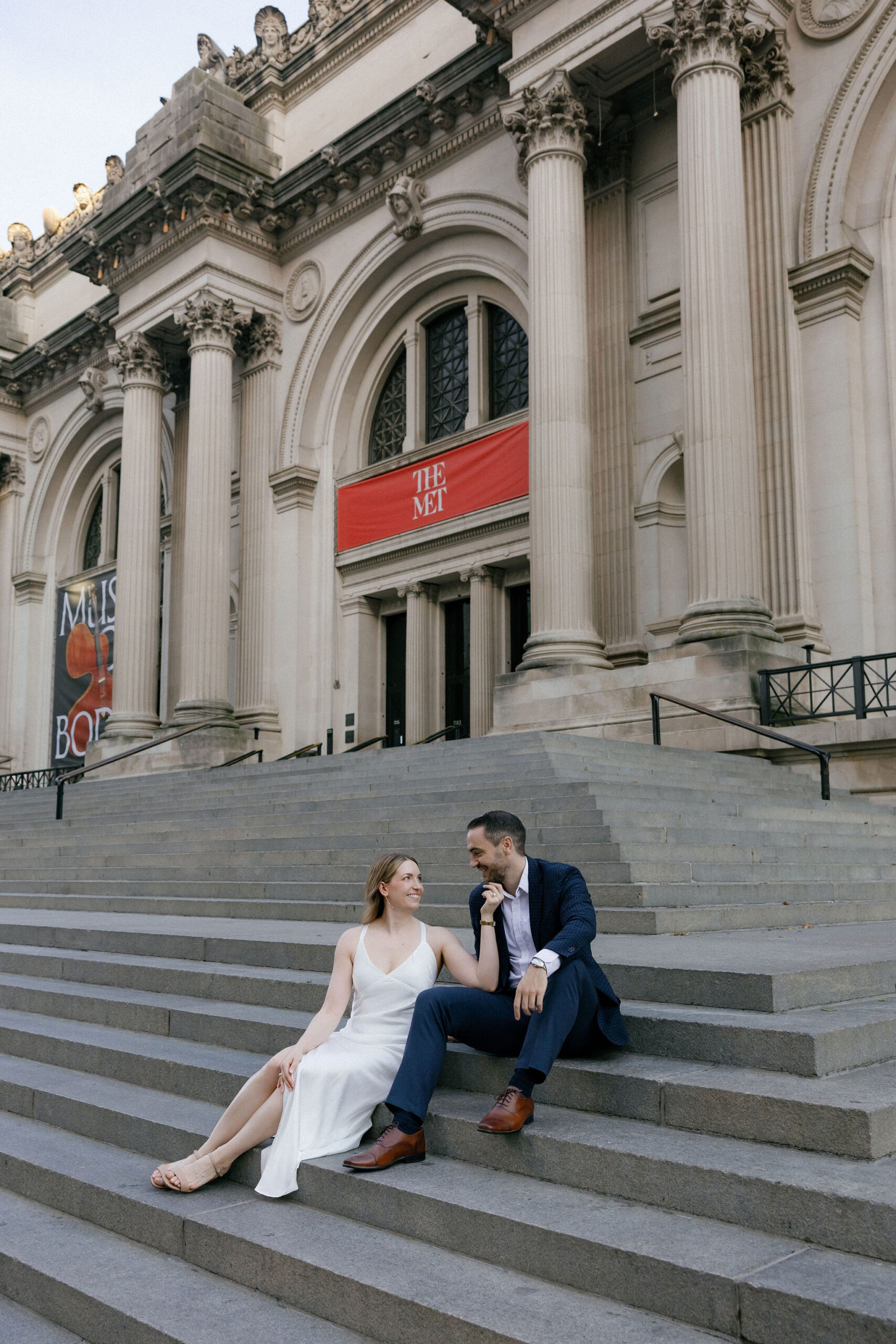 Engaged couple sitting together on The Met steps during their New York City engagement session.