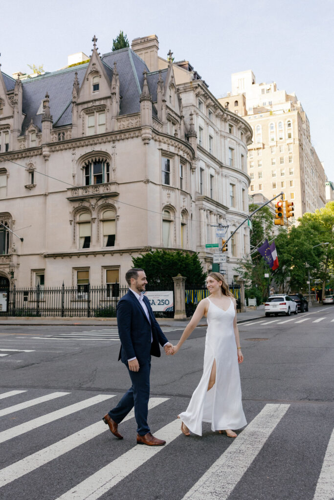 Engaged couple walking hand in hand through an Upper East Side crosswalk during their New York City engagement session.